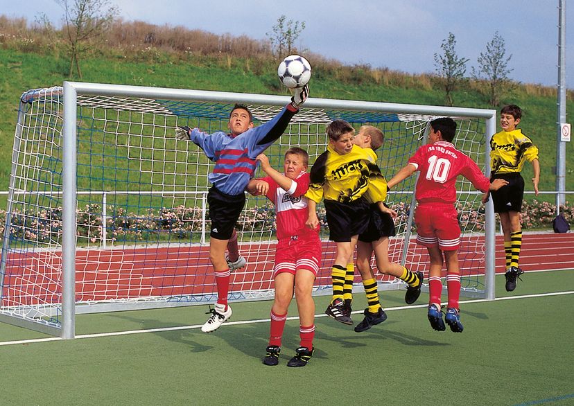 Jugendfußballtornetz, blau/weiß mit 6 Jungs in gelben Huck Trikots beim Fußball spielen